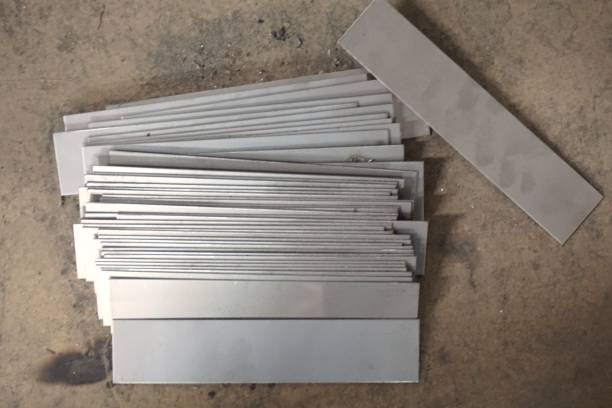 A stack of stainless steel flat bars arranged on a concrete floor, showcasing various widths and lengths. The polished surface of the bars highlights their industrial-grade quality